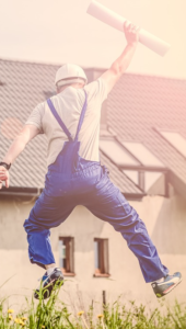 Construction worker in bibbled overalls, jumping with plans in hand